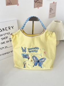 Detailed macro view of yellow canvas tote bag showing butterfly embroidery and plaid handles