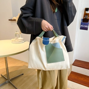 Detail view of cream canvas tote bag with green and blue leather pocket accents