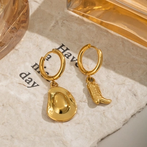 Gold asymmetric earrings featuring cowboy boot and hat charms on textured paper