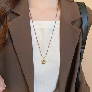 Detail of a vintage golden oval pendant with spiral texture on a brown wax cord necklace