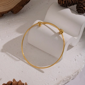 Adjustable gold stainless steel bracelet displayed on a white textured stand with pine cones