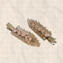 Detail view of two beige and grey flower hair clips with pink crystal embellishments