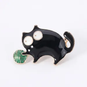 Close-up of black cartoon cat brooch with gold edges and green yarn ball on wood background