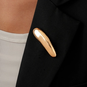 Polished gold-tone geometric teardrop brooch styled on a professional black blazer lapel