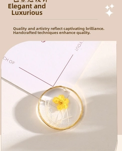 Close-up of a round gold alloy pendant with yellow dried flower in clear resin