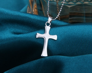 Détail d'un pendentif croix en argent avec chaîne à billes sur fond de soie bleue