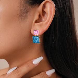 Detailed close-up of pink and blue geometric enamel earrings with textured gold trim