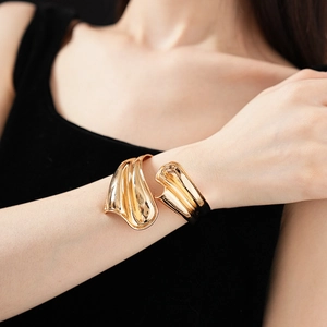 Detail of minimalist wavy gold metal cuff bracelet worn on wrist with black attire