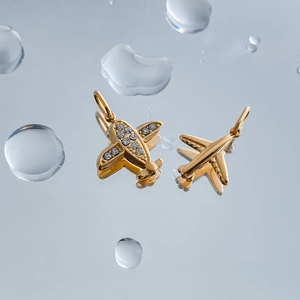 Macro detail of gold-plated airplane pendants with zircon inlay on water-reflective surface