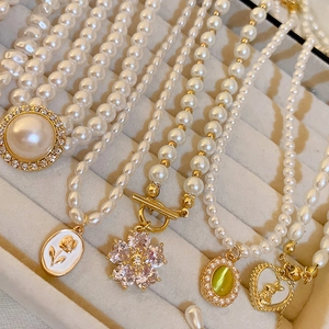 Détail de colliers de perles vintage français avec pendentifs dorés dans un écrin