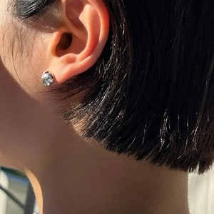 Close-up of a silver irregular lava-style stud earring worn on a model with sunlit shadows