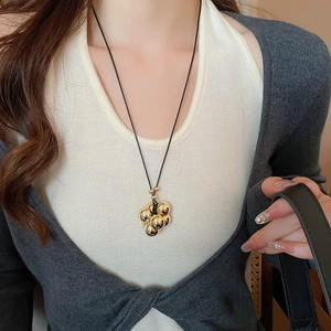 Dettaglio di una collana con ciondolo a grappolo di sfere dorate su un outfit casual