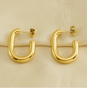 Detailed view of polished 18k gold U-shape stainless steel earrings on beige fabric