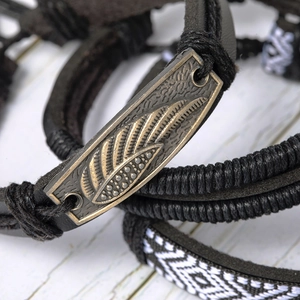 Detailed macro view of multilayer leather bracelet featuring a vintage bronze feather charm