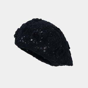 Detailed close-up of intricate crochet flower pattern on black cotton knit beret hat