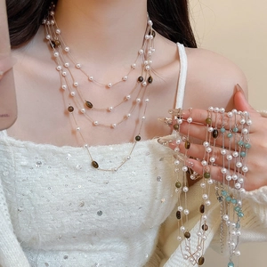 Dettaglio di collana a strati con perle bianche, grani marroni e catenina dorata su modella