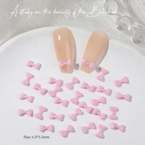 Detailed view of mini pink bow nail art charms sized 6.5x3.5mm on a white tray
