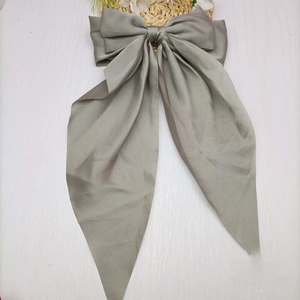 Detailed view of grey silk ribbon bow hair clip with elegant satin texture on white wood