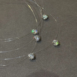Dettaglio di ciondoli rotondi in zircone su collane invisibili in filo di nylon