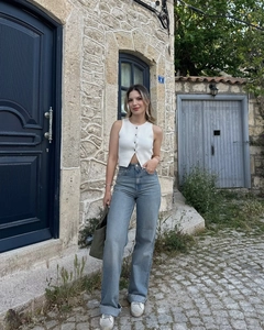 Détail d'un gilet blanc tricoté sans manches avec un jean bleu clair à jambes larges