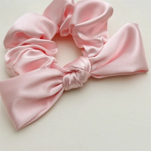 Close-up of pink satin scrunchie with silk bow detail showing smooth fabric texture