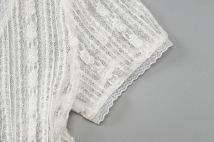 Dettaglio della manica in pizzo bianco con motivi floreali e finitura con bordo a onde