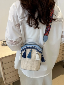 Detail of woven straw bucket bag with blue tassels and geometric pattern strap
