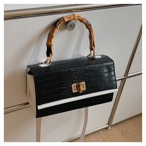Detail of black crocodile texture handbag with bamboo handle and golden clasp hardware