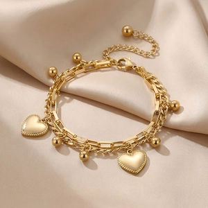 Detail of gold double-layer heart bracelet displayed on elegant champagne satin fabric