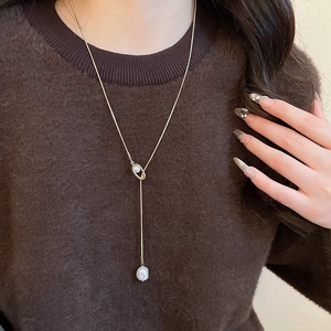 Detail of a gold heart-style pearl necklace worn over a stylish brown sweater
