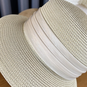 Detail of elegant beige woven straw hat with triple-layered cream satin ribbon trim