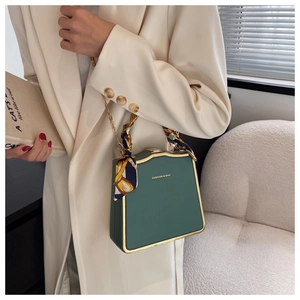 Detail of dark green square bag with gold trim, chain strap and silk scarf handle decor