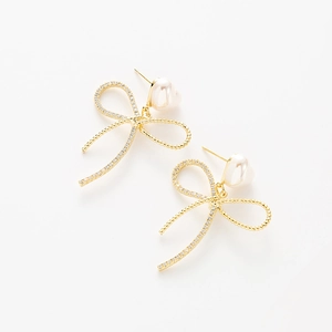 Close-up of golden bow earrings featuring sparkling pavé crystals and drop pearls
