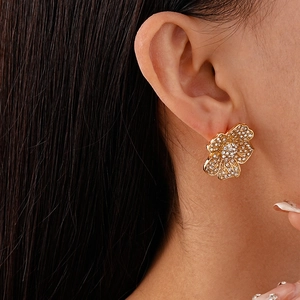 Close-up of elegant gold flower stud earrings with crystals on female model