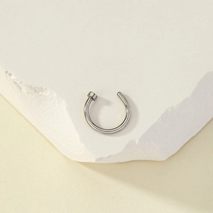 Detailed macro view of silver stainless steel C-shaped nose ring on white textured stone