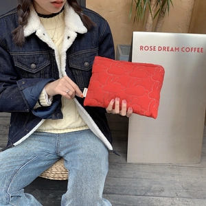 Quilted red bunny pattern makeup bag held by a model in a cozy cafe setting