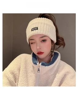 Detail view of a cream-white knitted beanie with black rectangular logo patch and text