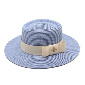 Detail of light blue straw boater hat with beige ribbon and golden bee metal ornament