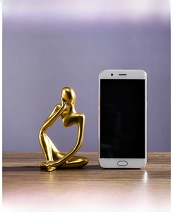 Golden abstract thinker statue on wood desk next to a smartphone for size scale