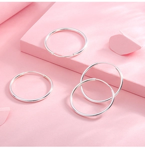 Close-up of four polished S999 sterling silver hoop earrings on a soft pink background