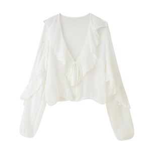 Detail of the ruffled V-neckline and tie-front closure on a white long-sleeve blouse