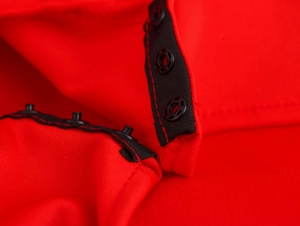 Detail of black plastic snap buttons on a red sleeveless dress with reinforced stitching