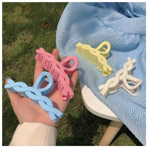 Close-up of four matte colorful twisted claw clips in pastel blue, pink, yellow, and white