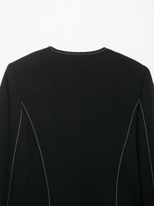 Close-up of contrast white stitching on a black textured blazer with precise collar detail