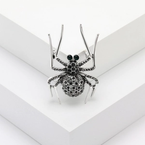 Vintage spider brooch with black crystals and green gemstone eyes on white pedestal