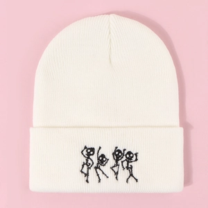 Détail du bonnet en tricot blanc avec quatre broderies de squelettes dansant sur le revers