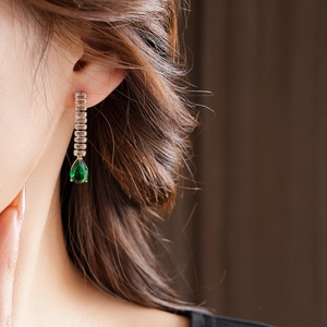 Close-up of elegant gold drop earrings with emerald stone and sparkling zircon accents