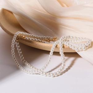 Elegant double-layer white faux pearl necklace with gold clasp on beige silk fabric