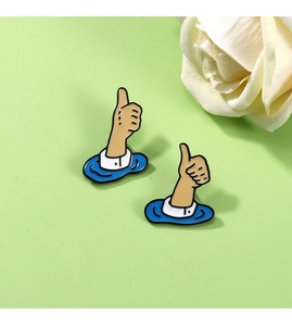 Detailed view of two cute cartoon thumb enamel brooches with gold plating on green surface