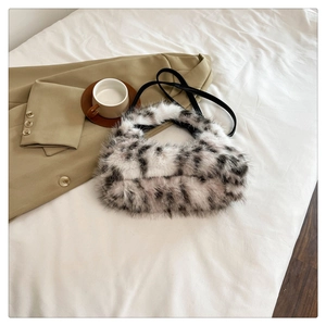 Close-up of plush crescent bag with animal print and black leather strap on white linen
